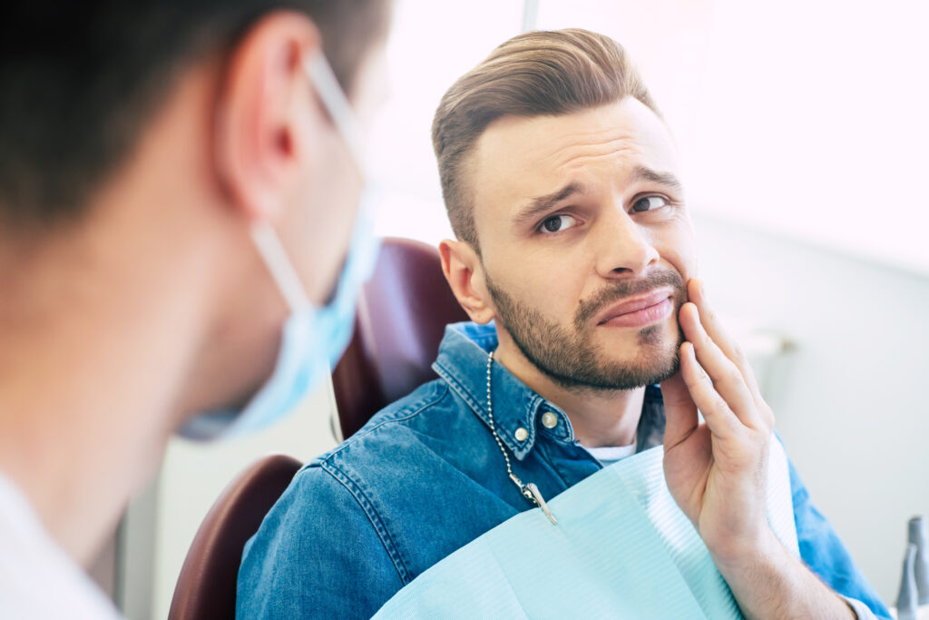 Symptoms of gums pain. A man with a worried face is holding his